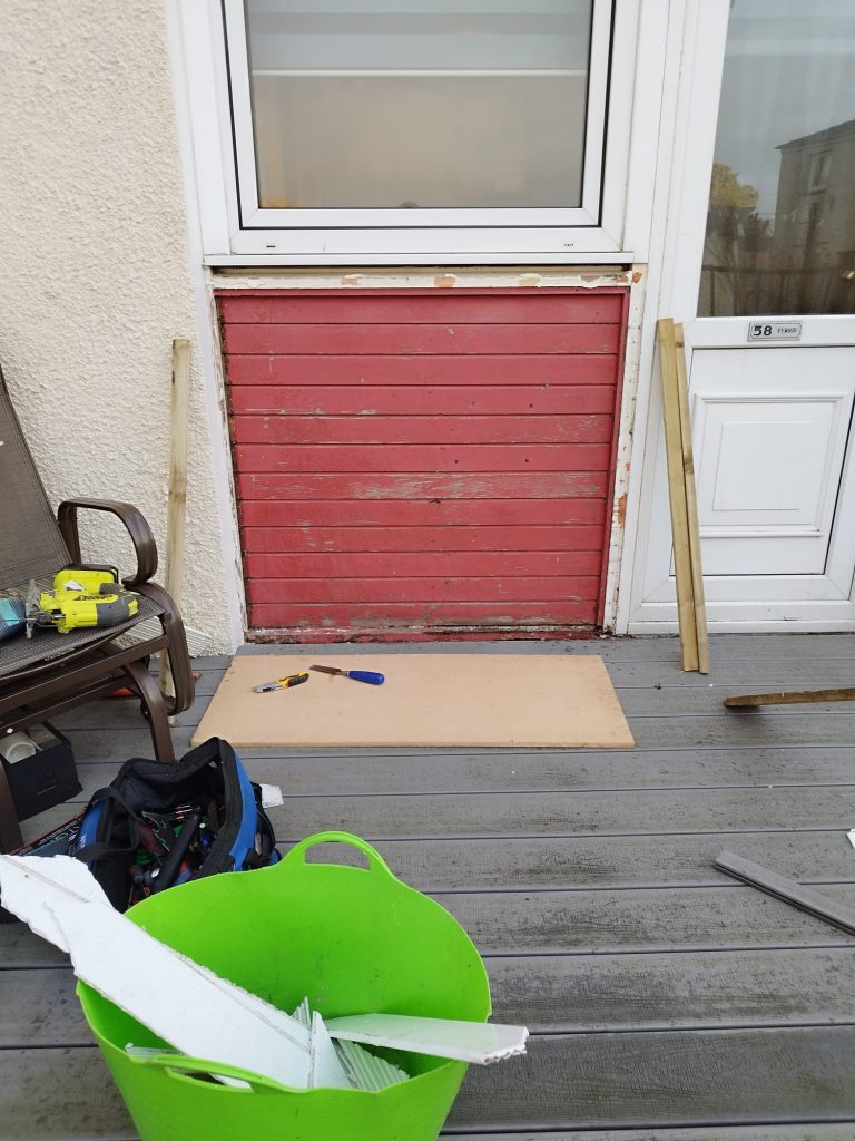 Weathered red timber panel beside a uPVC back door before the panel was replaced