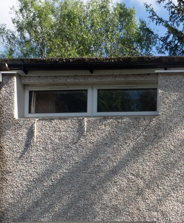 Tired old white uPVC window in a roughcast gable before replacement